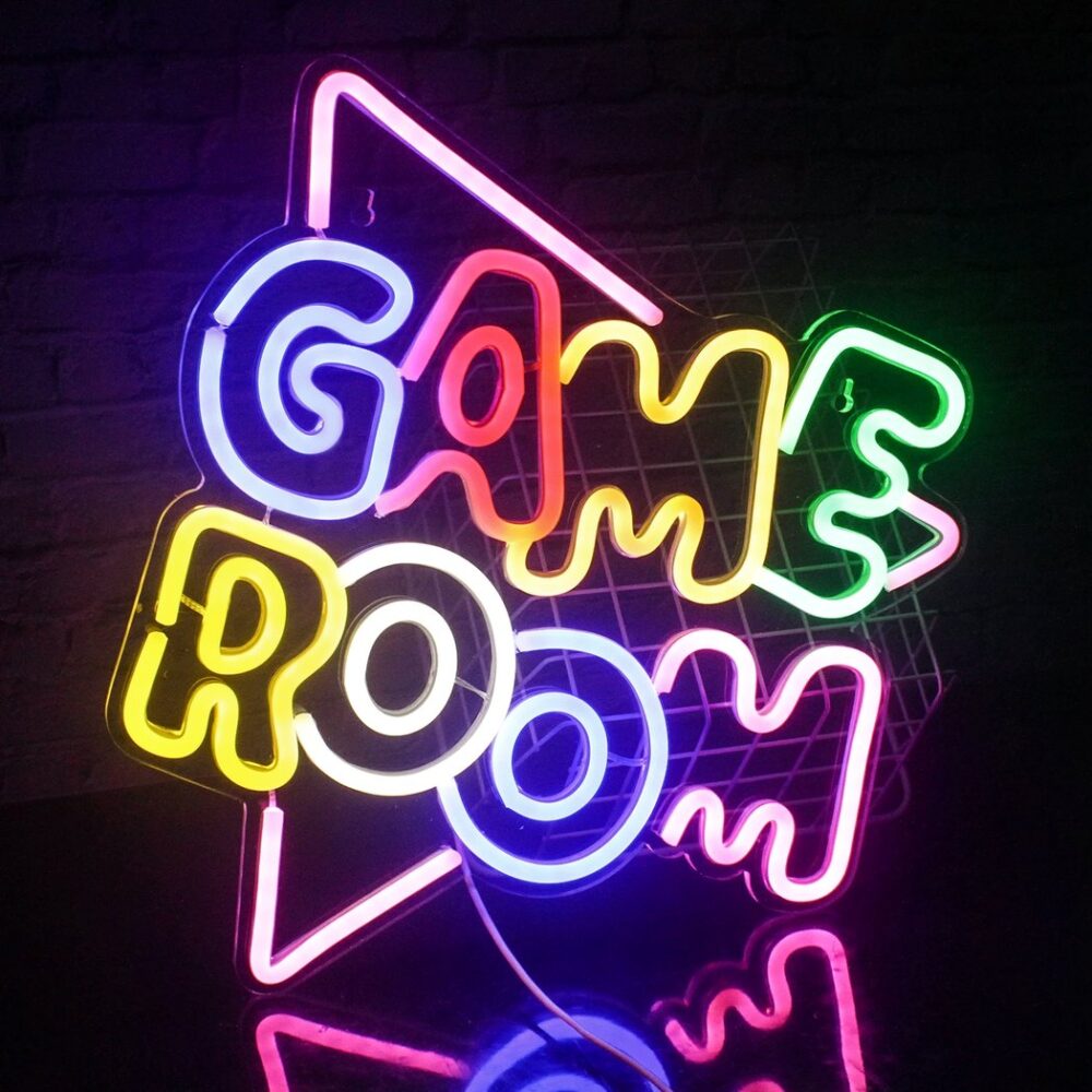 Beleuchtete Neon-Wandleuchte mit rosa Dreieck, auf dem GAME ROOM mit mehrfarbigen Buchstaben geschrieben steht.