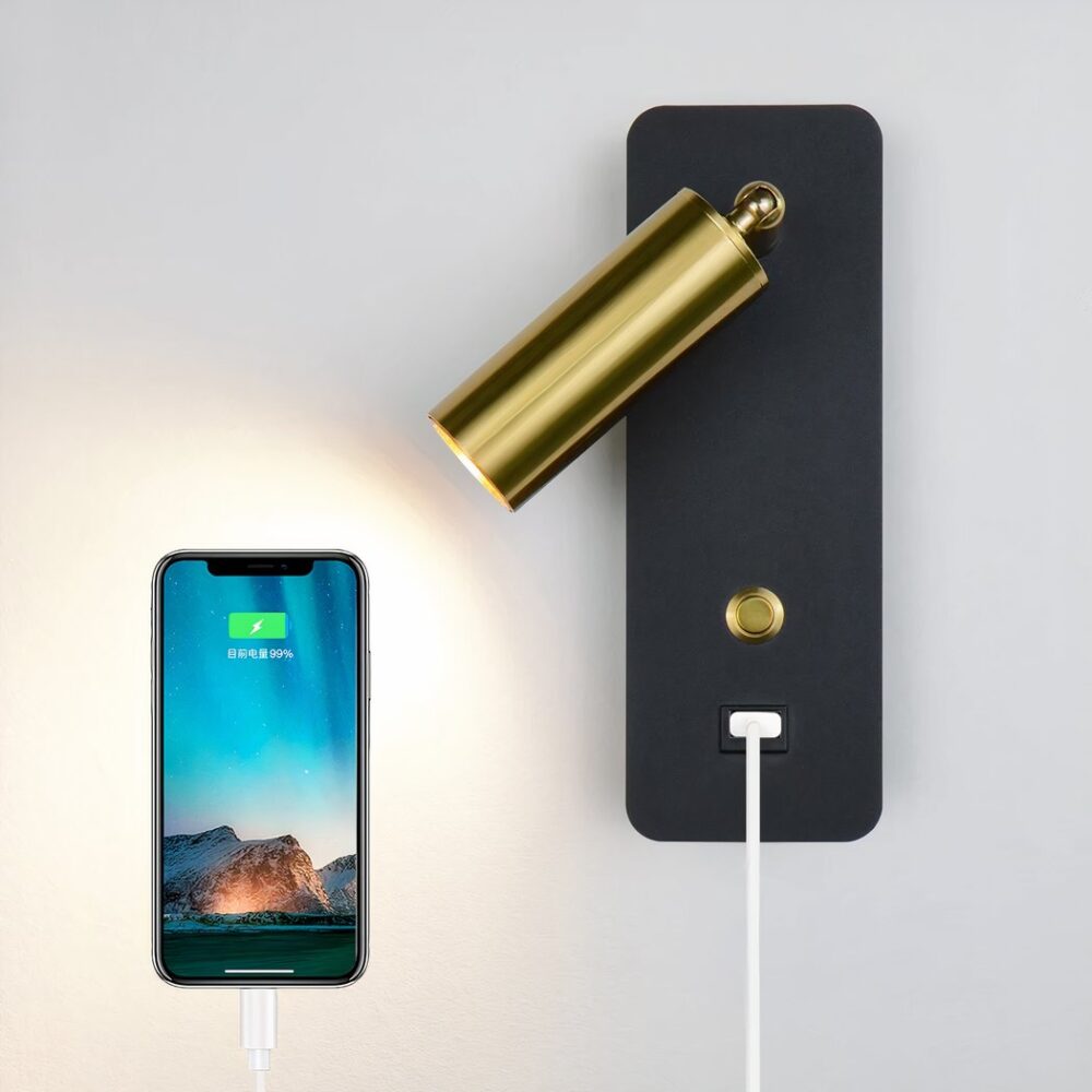 Verstellbare Wandleuchte mit schwarzer Halterung und goldenem Kopf, goldenem Schalter und USB-Anschluss. Daneben ein eingeschaltetes Smartphone, das mit einem weißen Kabel an die Wandleuchte angeschlossen ist.