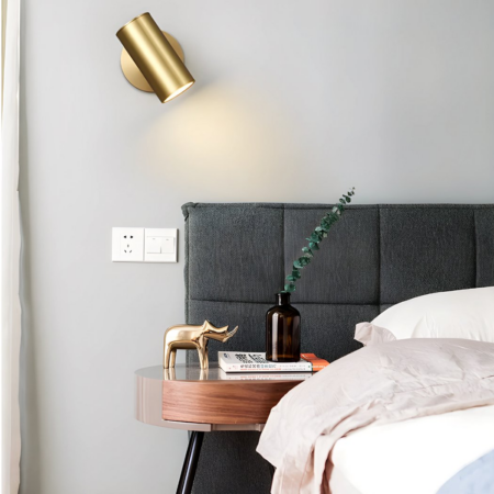 Goldene Wandleuchte aus Rohr mit einstellbarem Winkel hängt in einem Schlafzimmer