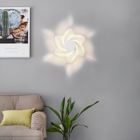 Wandleuchte in Form einer eingeschalteten Blume, die an einer grauen Wand befestigt ist. Links ein Gemälde und unten ein beigefarbenes Sofa mit einem gelben Kissen und rechts davon eine grüne Pflanze.