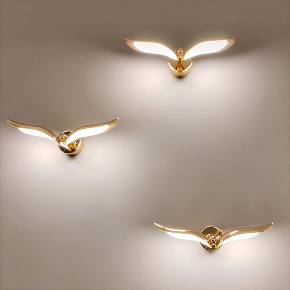 Graue Wand, an der 3 versetzte Wandleuchten in Form eines goldenen Vogels mit eingeschaltetem Licht in der Unterseite der Flügel angebracht sind.