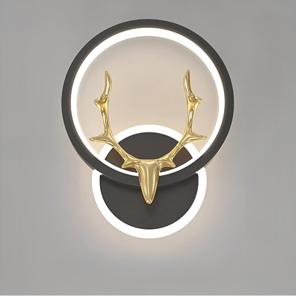 schwarze Wandleuchte, der Halter ist rund mit einem Lichtkreis darum herum. Er hält einen Lichtkreis in einem schwarzen Kreis, auf dem ein goldener Hirschkopf sitzt. Auf grauem Hintergrund.