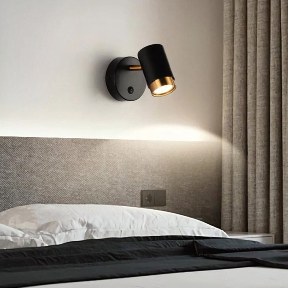 man sieht in einem grauen Zimmer über einem Kopfende des Bettes eine moderne schwarze Wandleuchte