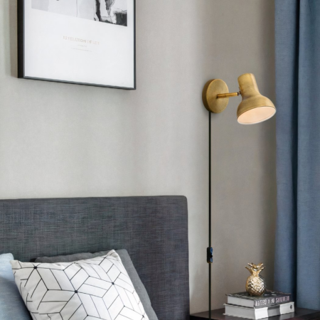 Verdrahtete Wandleuchte im Industriestil Eine verdrahtete Wandleuchte im Industriestil in Goldfarbe am Kopfende des Bettes