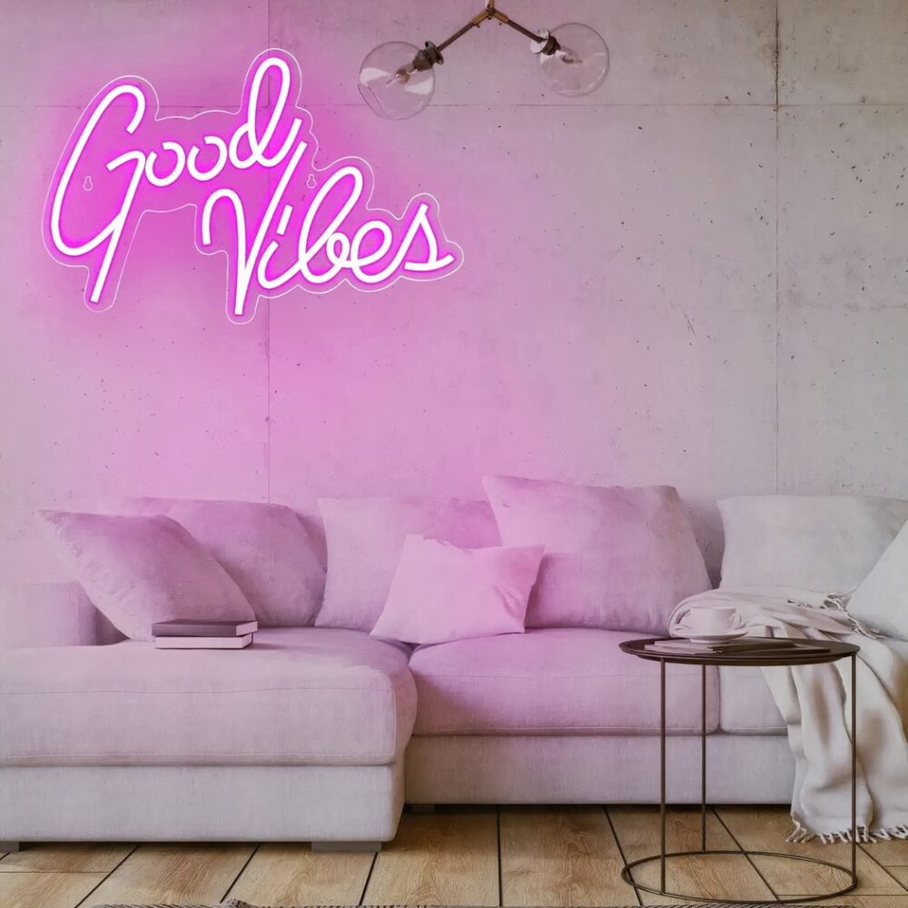 Neon-Wandleuchte good vibes eingeschaltet und an der Wand eines Wohnzimmers über einem großen beigen Ecksofa aufgehängt.