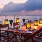 Solar-Wandleuchte mit flackerndem Flammeneffekt, die einen Tisch beleuchtet, an dem man draußen am Meer essen kann.