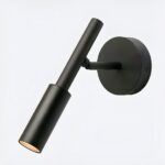 Schwarze Wandleseleuchte mit rundem Sockel und schwenkbarem Stab. LED ist eingeschaltet. Auf bläulichem Hintergrund.